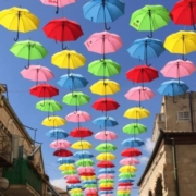 installation of umbrellas in many colors suspended in the air over a street in Jerusalem with blue sky in the background