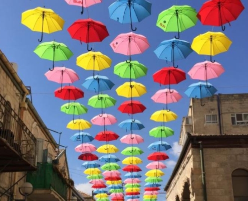 installation of umbrellas in many colors suspended in the air over a street in Jerusalem with blue sky in the background